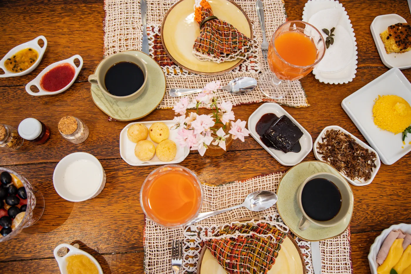 Mesa de café da manhã do Naim com café, sucos, cuscuz, tapioca, frutas e acompanhamentos.