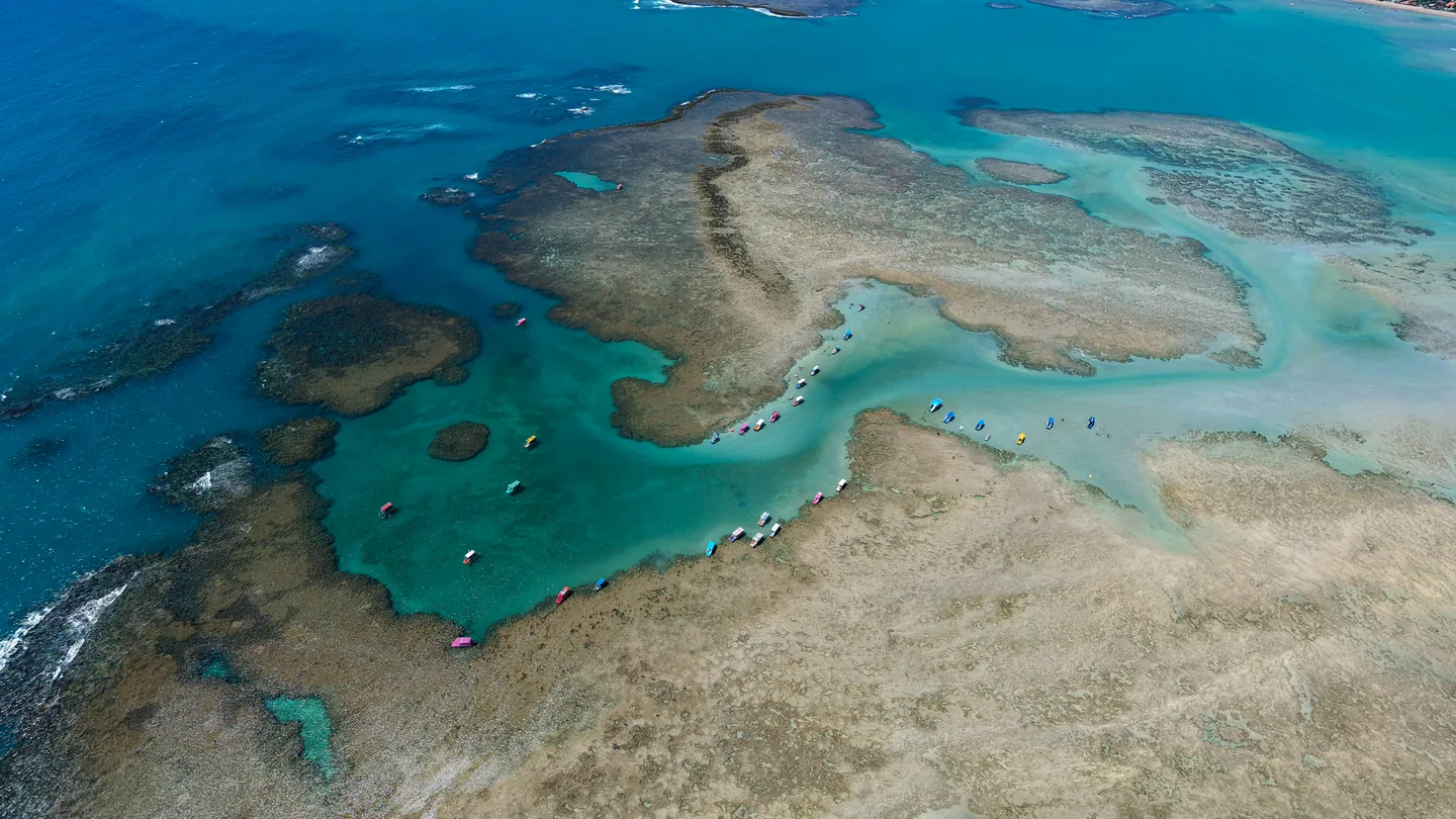 Vista aérea de piscinas naturais, recifes e jangadas no mar.